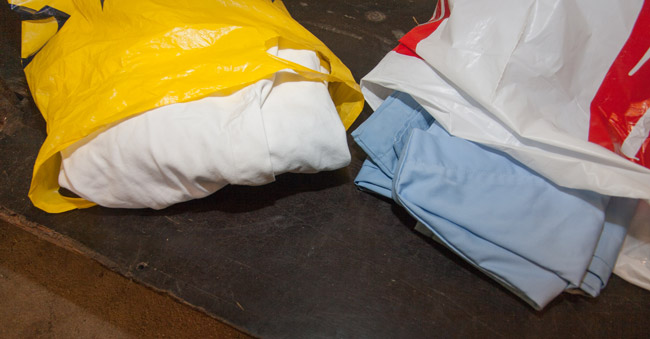 One blue scrub and a white lab coat in two different plastic bags 
